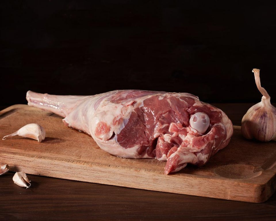 A raw lamb leg on a wooden cutting board with garlic cloves, showcasing Deadwood Farm's product.