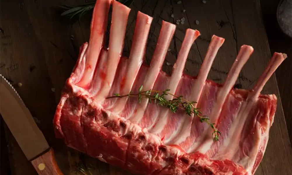 Raw rack of lamb with herbs and a knife on a wooden board, representing quality produce from Gingin Grass Fed.