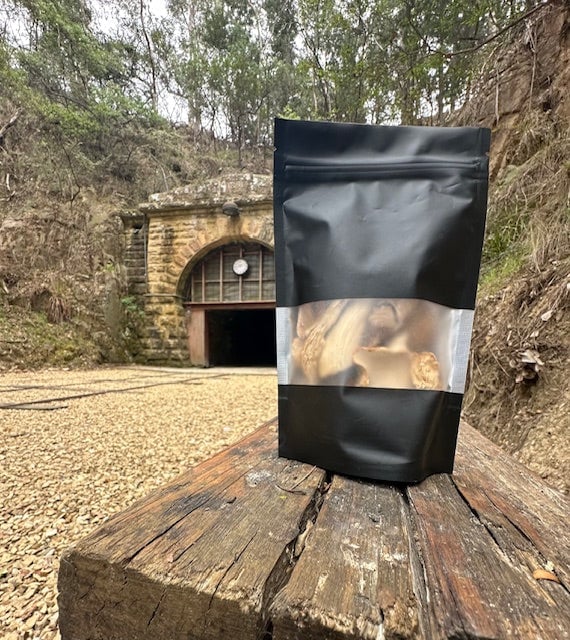 Black pouch of dried mushrooms from Tunnel Hill Mushrooms on a wooden beam, with the historic tunnel entrance in the background in Tasmania.