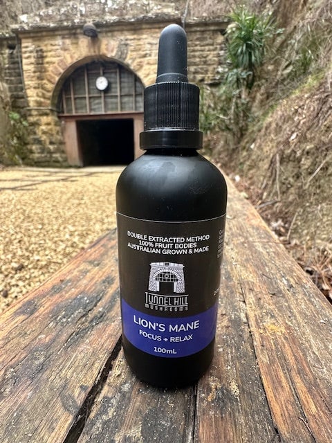 Bottle of Tunnel Hill Mushrooms Lion's Mane extract on a wooden beam, with the historic tunnel entrance in the background in Tasmania.