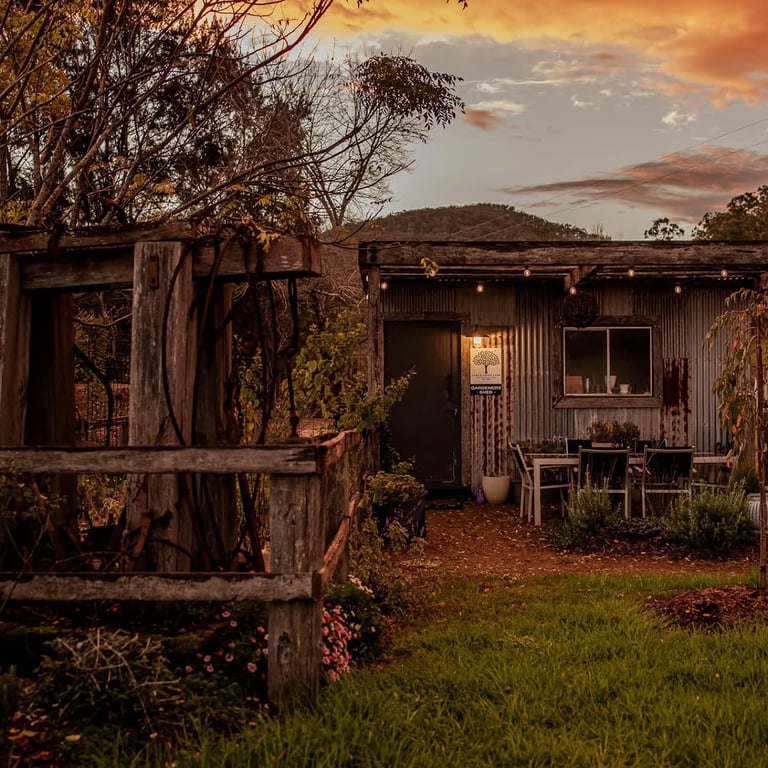 Rustic farm building with outdoor seating at Cedar Creek Farm Hunter Valley, bathed in a golden sunset glow.